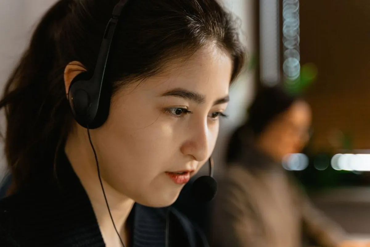 A Singapore customer service agent at a call station with headset, calm professional posture, monitor showing CRM record, focused listening expression