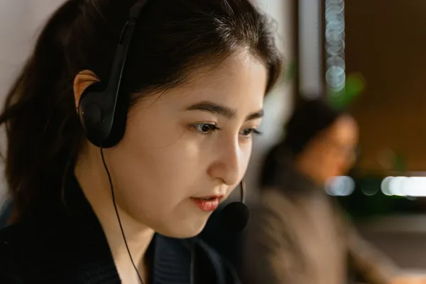 A Singapore customer service agent at a call station with headset, calm professional posture, monitor showing CRM record, focused listening expression