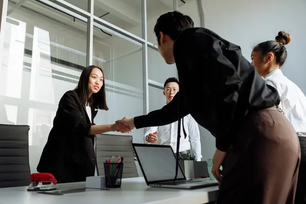A Singapore senior account manager and a long-standing client in a relaxed coffee meeting, both smiling, easy posture suggesting years of trust