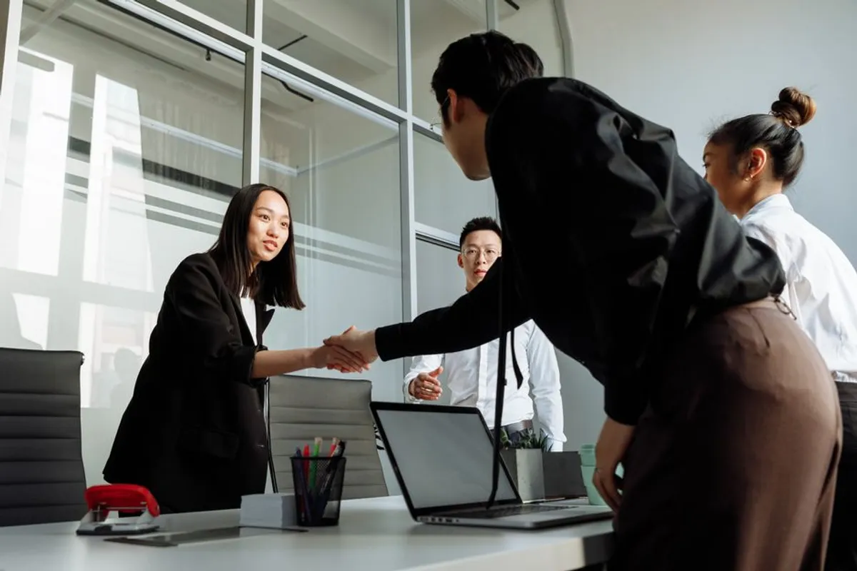 A Singapore senior account manager and a long-standing client in a relaxed coffee meeting, both smiling, easy posture suggesting years of trust