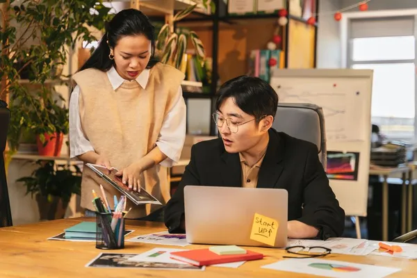 A Singapore professional preparing a structured status update on a laptop, with bullet points visible, calendar showing weekly cadence
