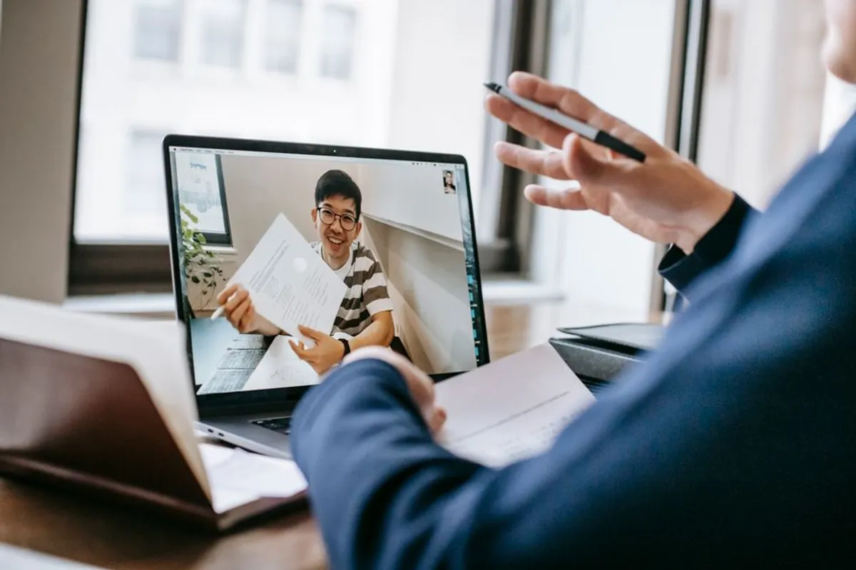 A Singapore professional presenting on Zoom from a well-lit home office, camera at eye level, laptop and second screen visible, professional posture