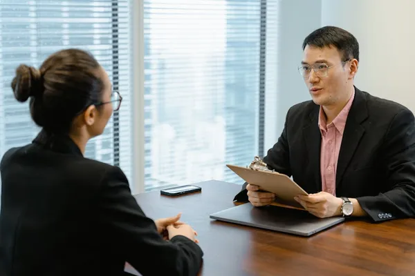 A Singapore professional in a calm one-to-one negotiation conversation across a desk, with documents and a calculator visible — composed, prepared, and respectful tone