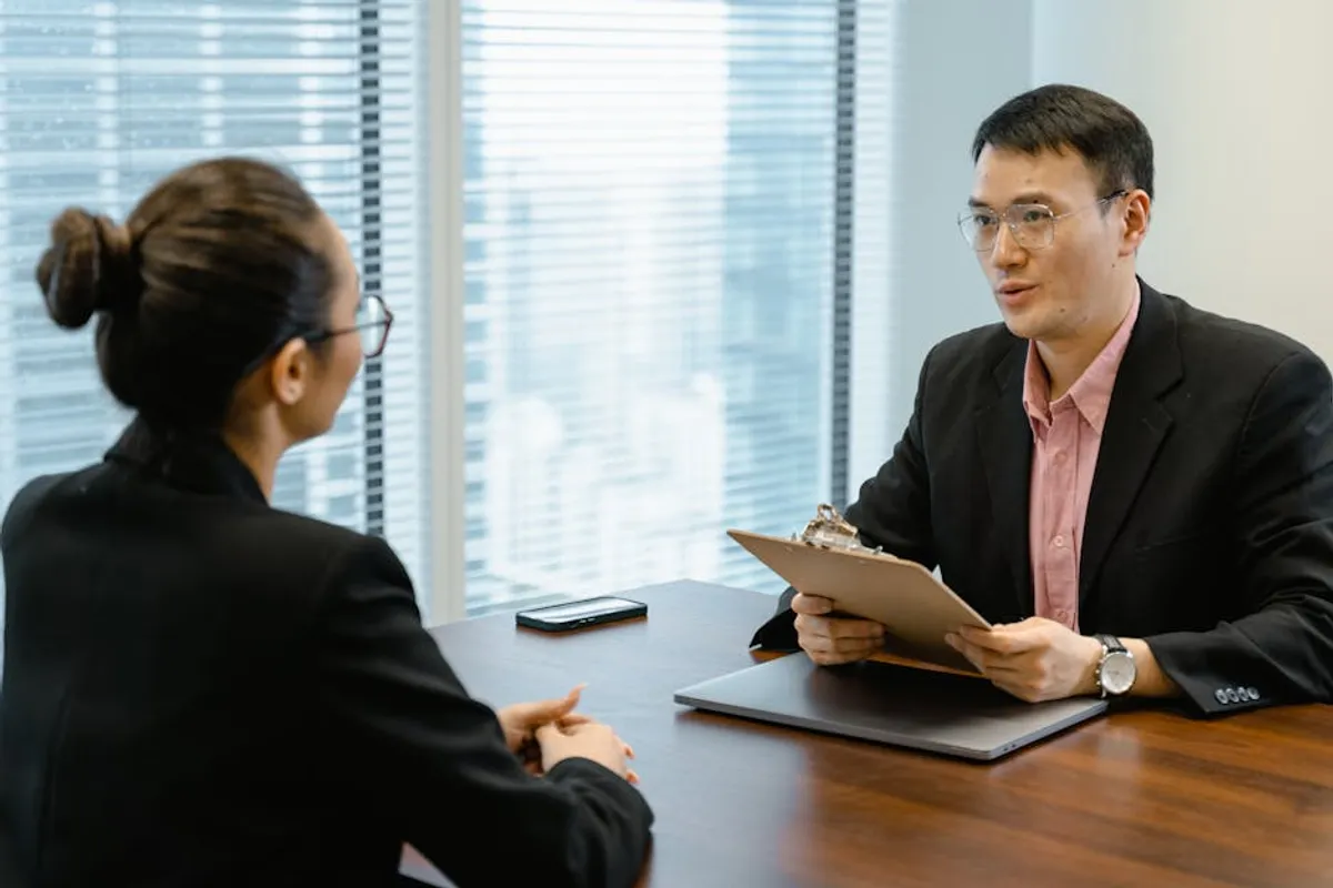 A Singapore professional in a calm one-to-one negotiation conversation across a desk, with documents and a calculator visible — composed, prepared, and respectful tone