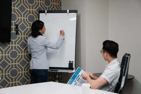 A Singapore presenter at the front of a meeting room mid-opening, audience attentive in the first 30 seconds, single slide visible behind