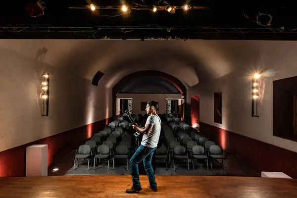 A speaker on a TEDx-style red circle stage with a single spotlight, simple presentation backdrop visible, audience in soft focus