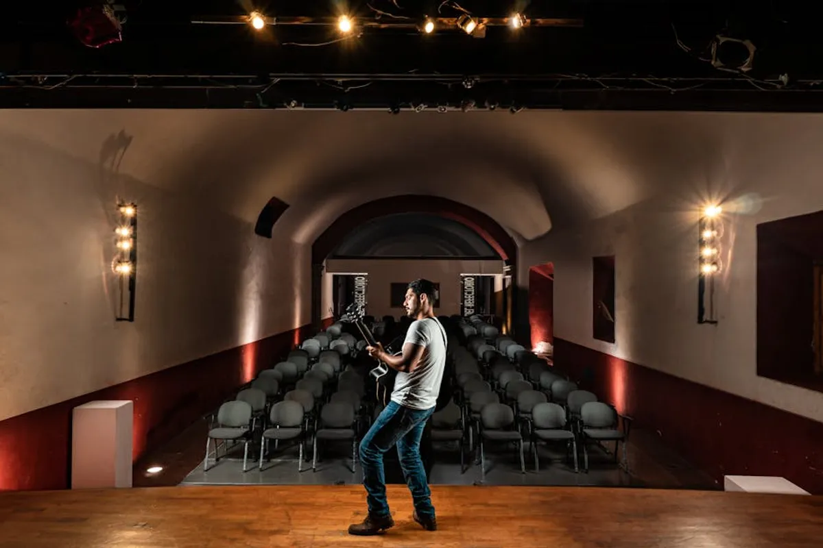 A speaker on a TEDx-style red circle stage with a single spotlight, simple presentation backdrop visible, audience in soft focus