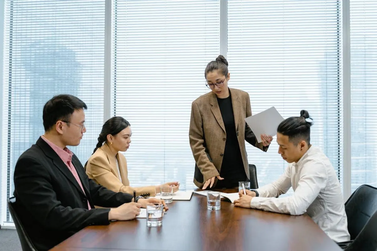 A Singapore manager presenting to a small group of senior leaders around a clean boardroom table — confident posture, one slide visible, attentive audience