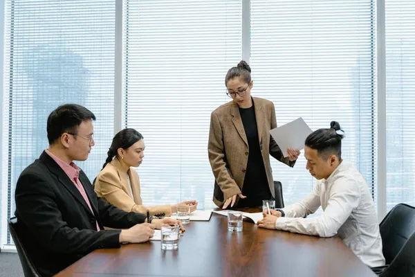 A Singapore manager presenting to a small group of senior leaders around a clean boardroom table — confident posture, one slide visible, attentive audience