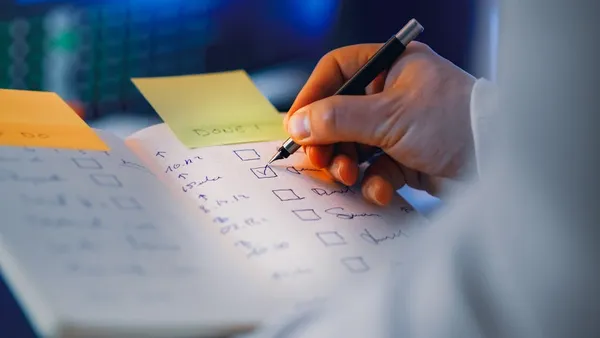 A Singapore professional triaging tasks on a paper notebook at a desk in the morning, with three priorities circled and a calendar visible