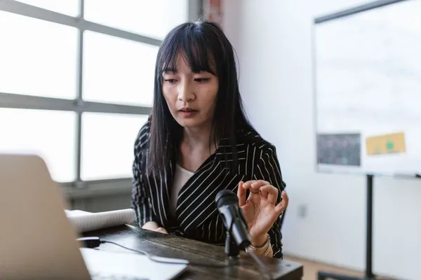 A Singapore speaker pausing deliberately mid-sentence at a meeting room — calm composure, audience listening, hand mid-gesture