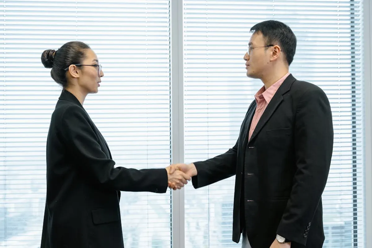 Two professionals at a negotiation table — one calm and listening, one mid-sentence — with notes face-down, suggesting careful information control