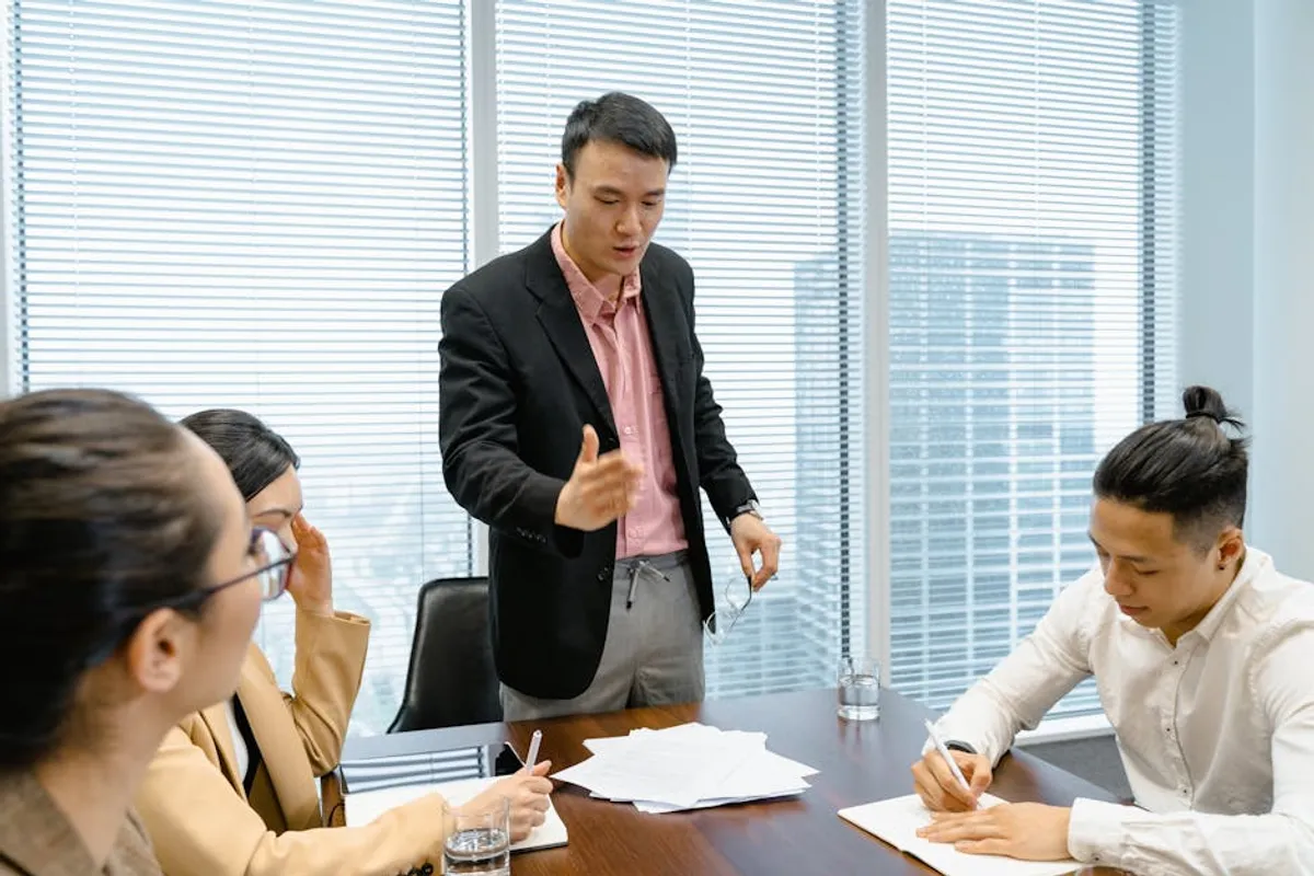 A Singapore B2B sales lead and a colleague reviewing a printed tender proposal at a clean desk, with a pricing spreadsheet and evaluation criteria visible