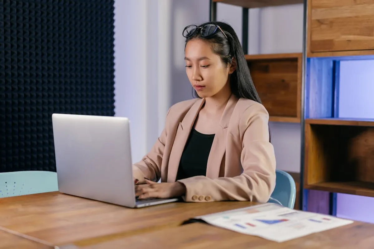 A Singapore manager drafting a budget request email at a desk with a financial spreadsheet and one-page business case visible alongside the laptop