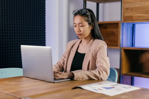 A Singapore manager drafting a budget request email at a desk with a financial spreadsheet and one-page business case visible alongside the laptop
