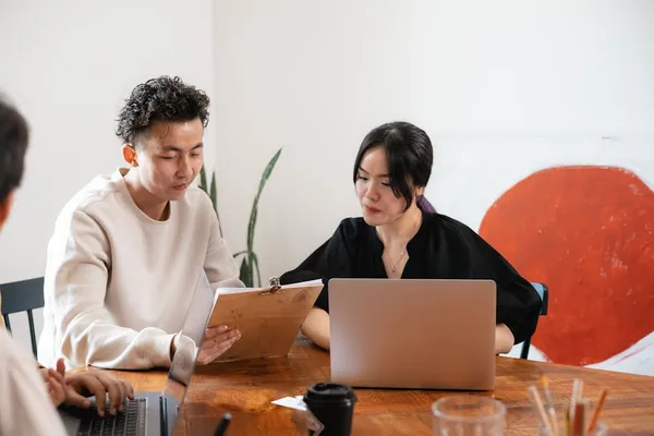 A Singapore professional drafting a meeting recap email immediately after a meeting, with handwritten notes and laptop open at a clean desk