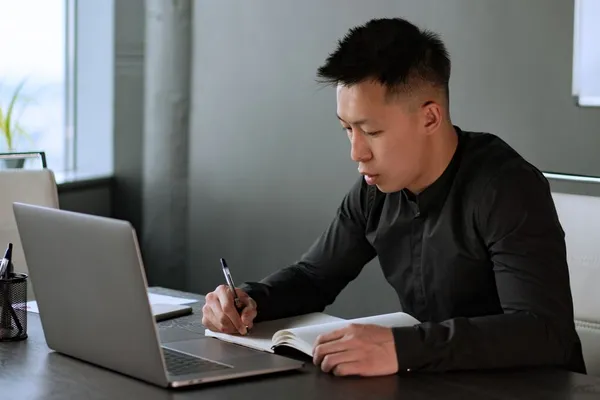 A Singapore professional editing their resume on a laptop with a printed copy alongside, marking specific achievements and numbers in red pen