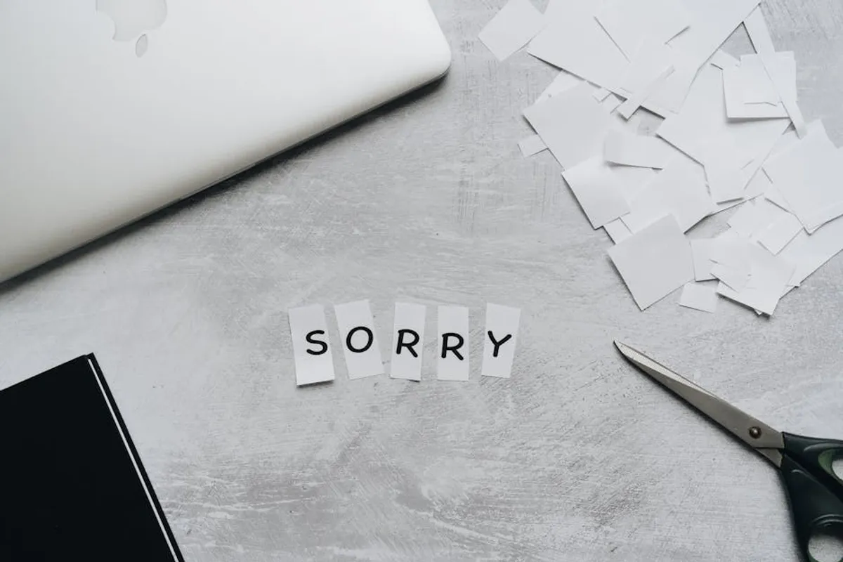 A Singapore professional carefully drafting an apology email at a clean desk, paused mid-thought, a printed copy of the original error on the desk