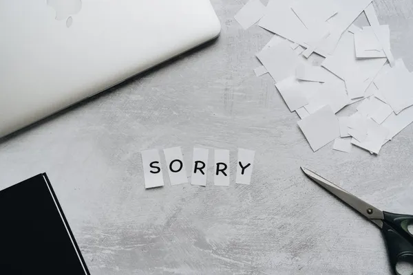 A Singapore professional carefully drafting an apology email at a clean desk, paused mid-thought, a printed copy of the original error on the desk